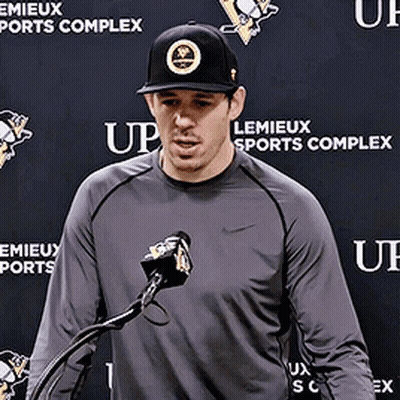 A Man Stands In Front Of A Microphone In Front Of A Wall That Says Lemieux Sports Complex GIF
