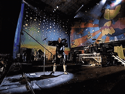 A Man Stands In Front Of A Microphone On A Stage With A Colorful Background GIF