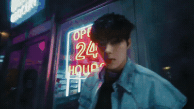 A Man Stands In Front Of A Neon Sign That Says 24 Hours GIF