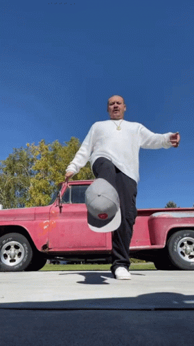 A Man Stands In Front Of A Pink Truck Holding A Hat That Says ' Ford ' On It GIF