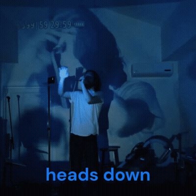 A Man Stands In Front Of A Projection Of A Woman And The Words Heads Down GIF