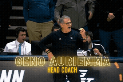 A Man Stands In Front Of A Sign That Says Geno Auriemma GIF