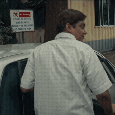 A Man Stands In Front Of A Sign That Says No Parking Vehicles Driven And Parked Inside The Premises At Owners Risk GIF