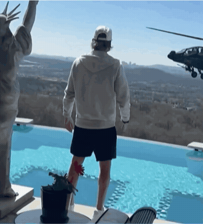 A Man Stands In Front Of A Statue Of Liberty And A Helicopter Flying Overhead GIF