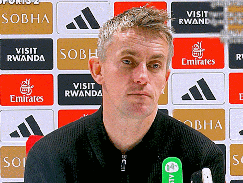 A Man Stands In Front Of A Wall That Says " Visit Rwanda " And " Emirates " GIF