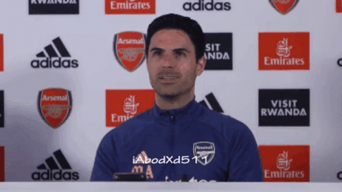 A Man Stands In Front Of A Wall With Arsenal And Emirates Logos GIF