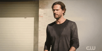 A Man Stands In Front Of A Wall With The Letters Cw On The Bottom GIF