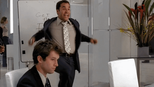 A Man Stands In Front Of A White Board That Says Get The GIF