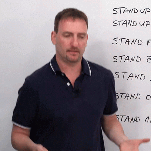 A Man Stands In Front Of A White Board That Says Stand Up Stand Up Stand F Stand B Stand C Stand O And Stand A GIF