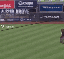 A Man Stands On A Baseball Field With A Sign That Says Coupa On It GIF