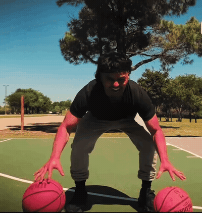 A Man Stands On A Basketball Court Holding Two Pink Basketballs One Of Which Has The Number 13 On The Back GIF