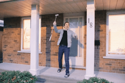 A Man Stands On A Porch Holding A Remote Control In Front Of A House With The Number 18 On It GIF