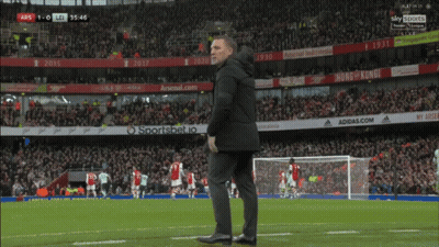 A Man Stands On A Soccer Field With Ads For Adidas.com And Arsenal.com In The Background GIF
