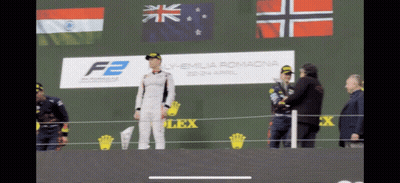 A Man Stands On A Stage In Front Of A Sign That Says F2 On It GIF