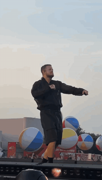 A Man Stands On A Stage In Front Of Beach Balls GIF
