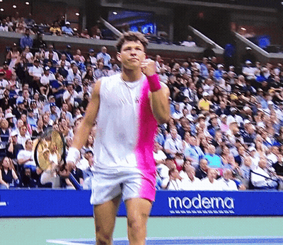 a man stands on a tennis court with a moderna banner behind him