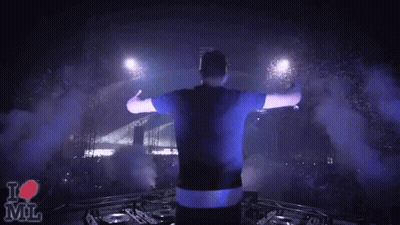 A Man Stands On Stage With His Arms Outstretched In Front Of A Crowd And A Sign That Says " I Love Mil " GIF