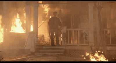 A Man Stands On The Porch Of A House That Is On Fire GIF
