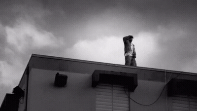 A Man Stands On The Roof Of A Building Looking Up At The Sky GIF