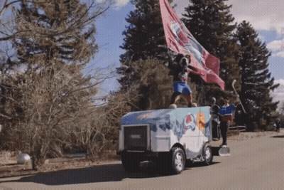A Man Stands On Top Of An Ice Hockey Vehicle With A Flag Flying In The Wind GIF