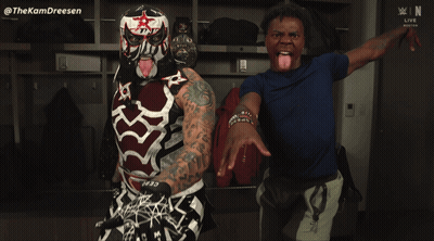 A Man Sticking His Tongue Out Next To A Wrestler With A Mask On GIF