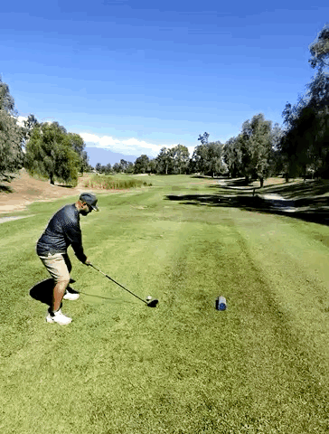 A Man Swings A Golf Club At A Golf Ball On A Golf Course GIF