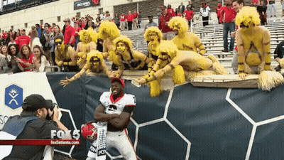 A Man Taking A Picture Of A Football Player In Front Of A Fox 5 Banner GIF