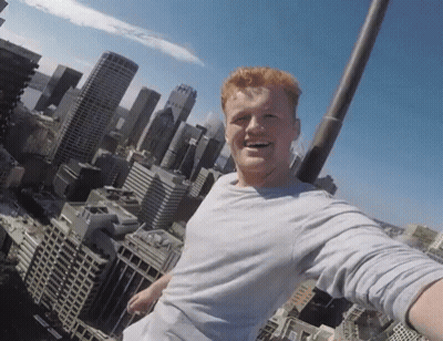 A Man Taking A Selfie On Top Of A Building With A City Skyline In The Background GIF
