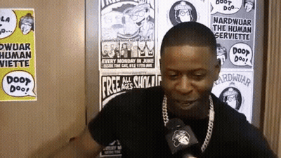 A Man Talking Into A Microphone In Front Of A Wall With Posters On It That Say Door Doo GIF