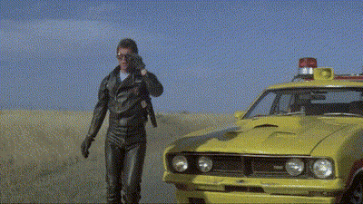 A Man Talking On A Cell Phone Next To A Yellow Car With A Red Light On Top GIF