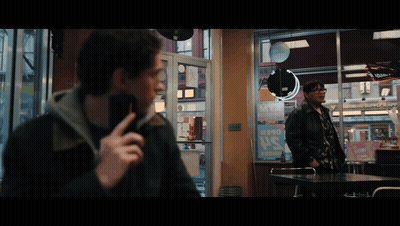 A Man Talking On A Cell Phone While Another Man Stands In Front Of A Sign That Says ' Pepsi ' On It GIF