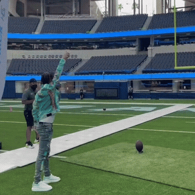 A Man Throws A Football On A Field With A Flag That Says Nfl GIF