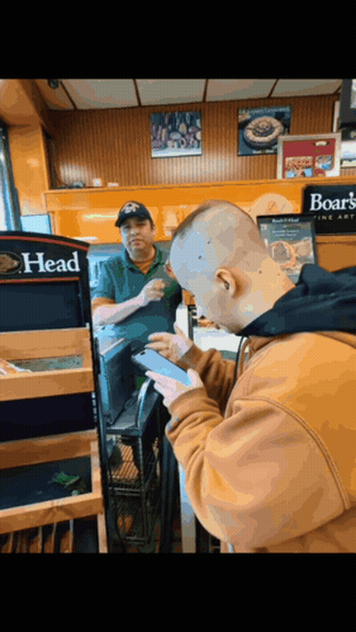 A Man Using A Cell Phone In Front Of A Sign That Says Boar 'S Head GIF