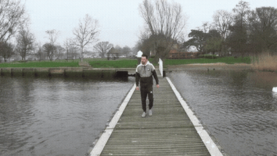 A Man Walking Across A Wooden Bridge Over Water GIF