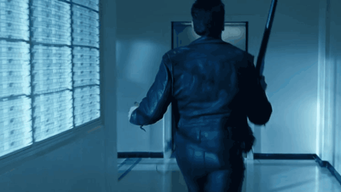 A Man Walking Down A Hallway Holding A Bat GIF