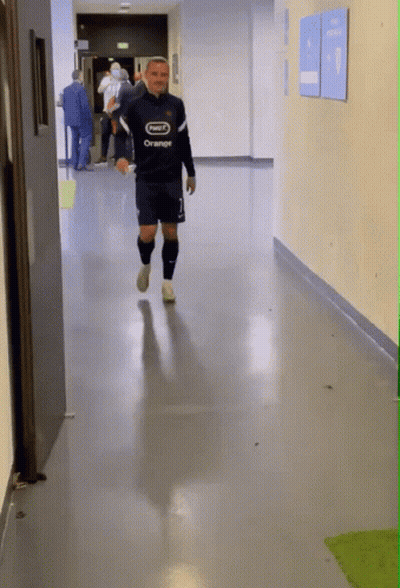 A Man Walking Down A Hallway With A Shirt That Says Orange On It GIF