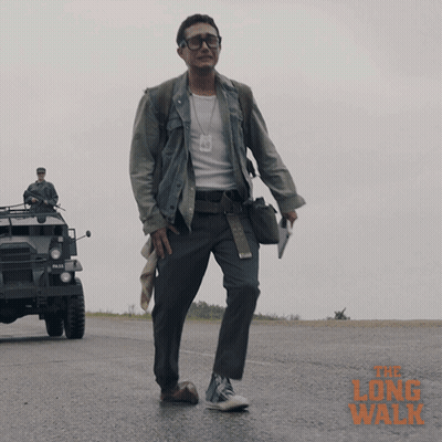 A Man Walking Down A Road With The Long Walk Written In Orange GIF