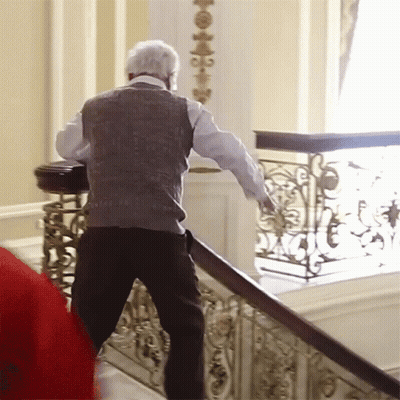 A Man Walking Down A Set Of Stairs With A Wrought Iron Railing Behind Him GIF