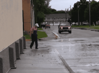 A Man Walking Down A Sidewalk In The Rain With A Red Truck Behind Him GIF