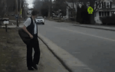 A Man Walking Down A Street With A Car Behind Him And A Yellow Sign That Says Right Turn GIF