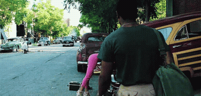 A Man Walking Down A Street With A Green Bag On His Back GIF
