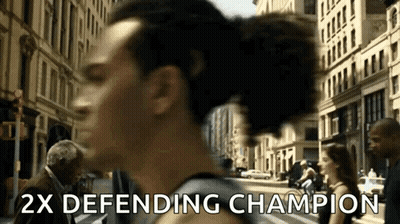 A Man Walking Down A Street With The Words " 2X Defending Champion " Written On The Bottom GIF