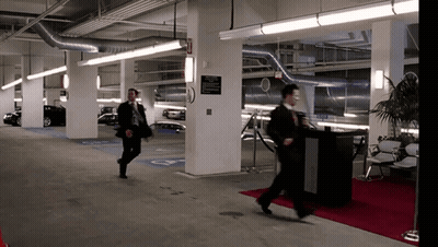 A Man Walking In A Parking Garage With A Sign On The Wall That Says ' Exit ' GIF