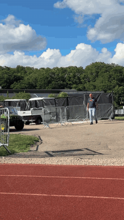 A Man Walking On A Track In Front Of A Fence With A Jeep In The Background GIF