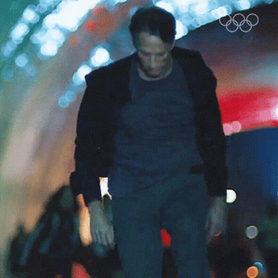 A Man Walking Through A Tunnel With The Olympic Rings On The Wall Behind Him GIF