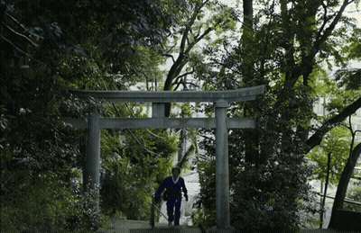 A Man Walking Up A Set Of Stairs Under A Torii Gate With Trees In The Background GIF