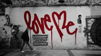 A Man Walks Past A Wall That Has Graffiti On It That Says Love GIF