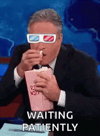 A Man Wearing 3D Glasses Is Eating Popcorn And Saying `` Waiting Patiently '' . GIF