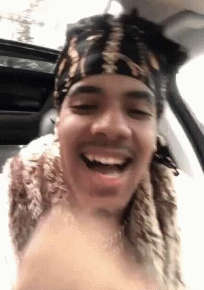 A Man Wearing A Bandana And A Fur Coat Is Sitting In A Car And Smiling . GIF