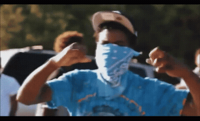 A Man Wearing A Bandana And A Hat Is Making A Fist In The Air . GIF